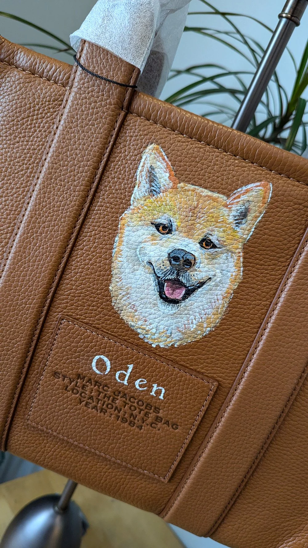 A brown leather tote bag with a detailed embroidered image of a smiling Shiba Inu dog on the front. Below the dog, the word 'Oden' is embroidered, and underneath that, there is smaller text describing the bag as a tote bag from Japan.