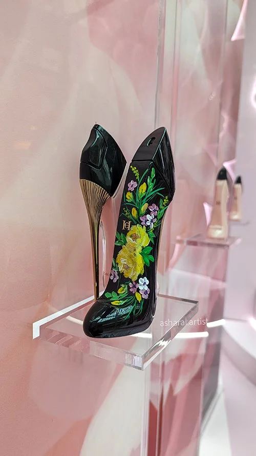 Carolina Herrera perfume bottle featuring hand-painted yellow roses, created live by AshaRai, luxury event artist, at the Carolina Herrera pop-up at Square One Shopping Centre in Mississauga.