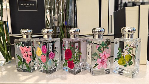 Five Jo Malone perfume bottles with floral designs on clear glass, live luxury event artist. Bottle painting at Yorkdale