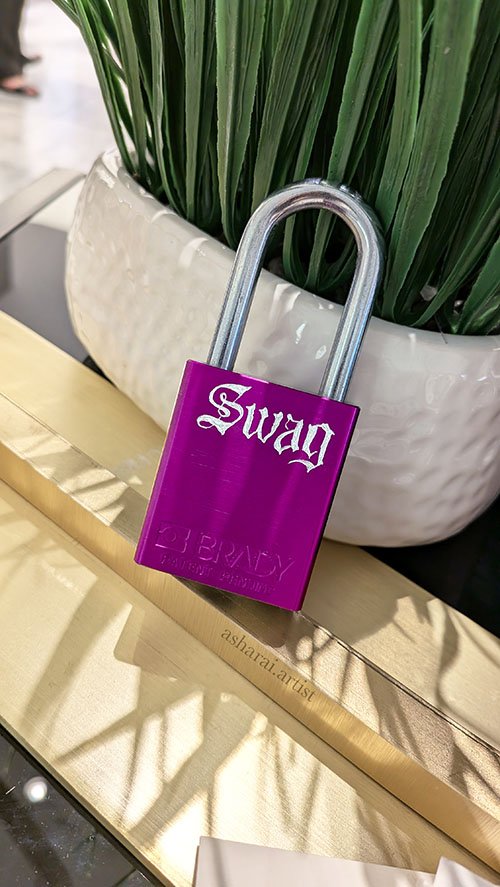 A purple metal surface padlock with the word 'Swag' hand engraved in a gothic font.