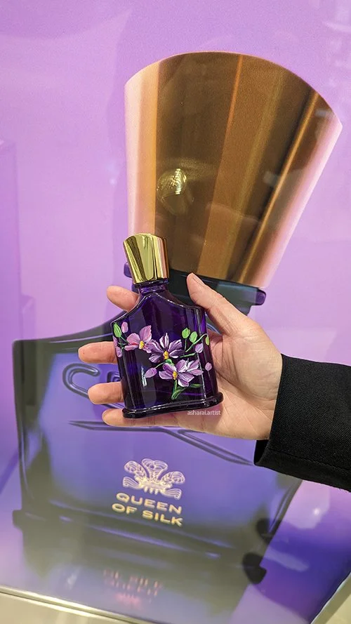 Creed Queen of Silk perfume bottle featuring hand-painted purple orchids, bottle painting by AshaRai, luxury event artist, at Holt Renfrew.
