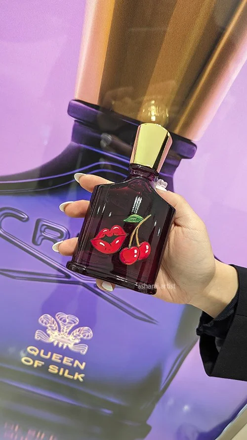 Creed Queen of Silk perfume bottle featuring a hand-painted design of red cherries and lips, created live by a luxury event artist at the Holt Renfrew fragrance launch.