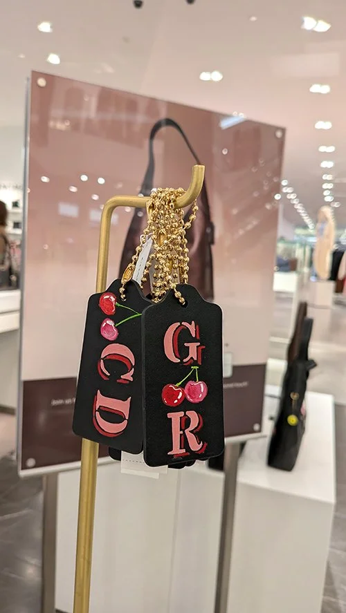 Fashion tags with cherries and the words "GIRL" and "QID" hanging on a clothing store display stand.