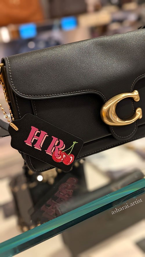Coach handbag with gold clasp and a tag featuring pink 'H R' and red cherries on a gold chain. Leather painting. Custom painting