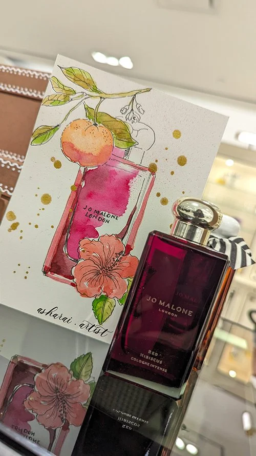 Jo Malone Red Hibiscus bottle featuring hand-painted hibiscus flowers and orange accents, created live by AshaRai, Toronto event artist and live engraver, at Holt Renfrew Yorkdale.