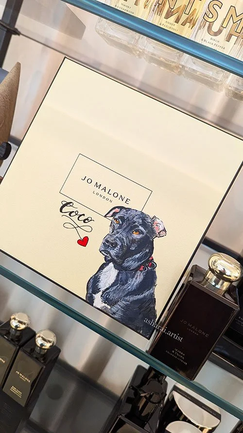 A Jo Malone London Perfume Box painted with a  realistic illustration of a black dog with a red collar and a small red heart, with the word 'Coco' next to it. Live events artist ,bottle painter Asha Rai