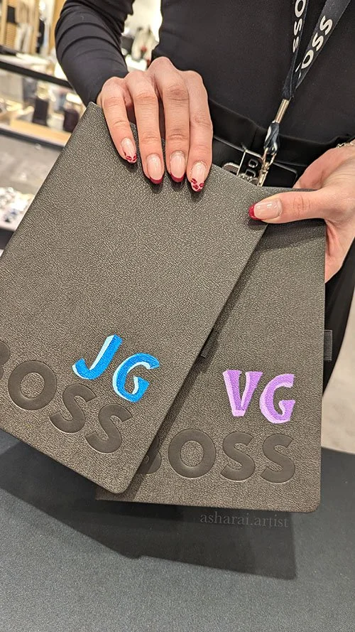 HUGO BOSS notebooks personalized with hand-painted initials on leather for a VIP in-store activation, showcasing custom live leather painting for luxury brand events.