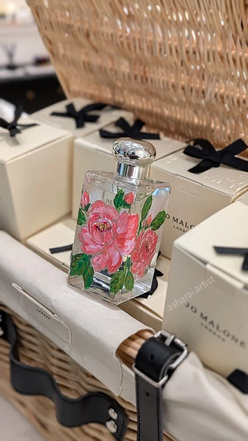 Jo Malone perfume bottle featuring hand-painted pink flowers and green leaves, showcasing live bottle painting by an event artist at Yorkdale.