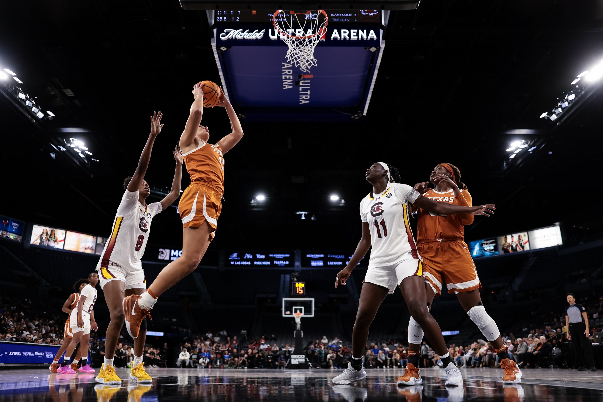 Women basketball players from Texas and South Carolina competing for the ball during a game at Michelob Ultra Arena, with spectators in the background.