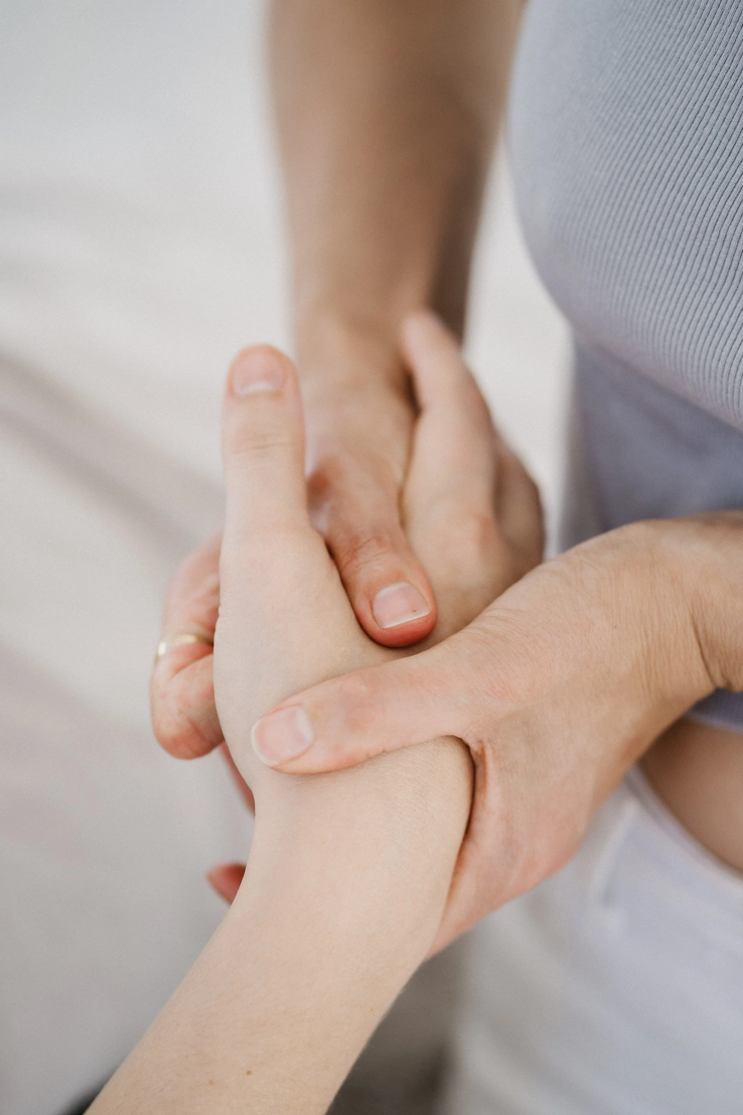 Close-up of two people holding hands, one with a darker skin tone and the other with a lighter skin tone, against a blurred background.