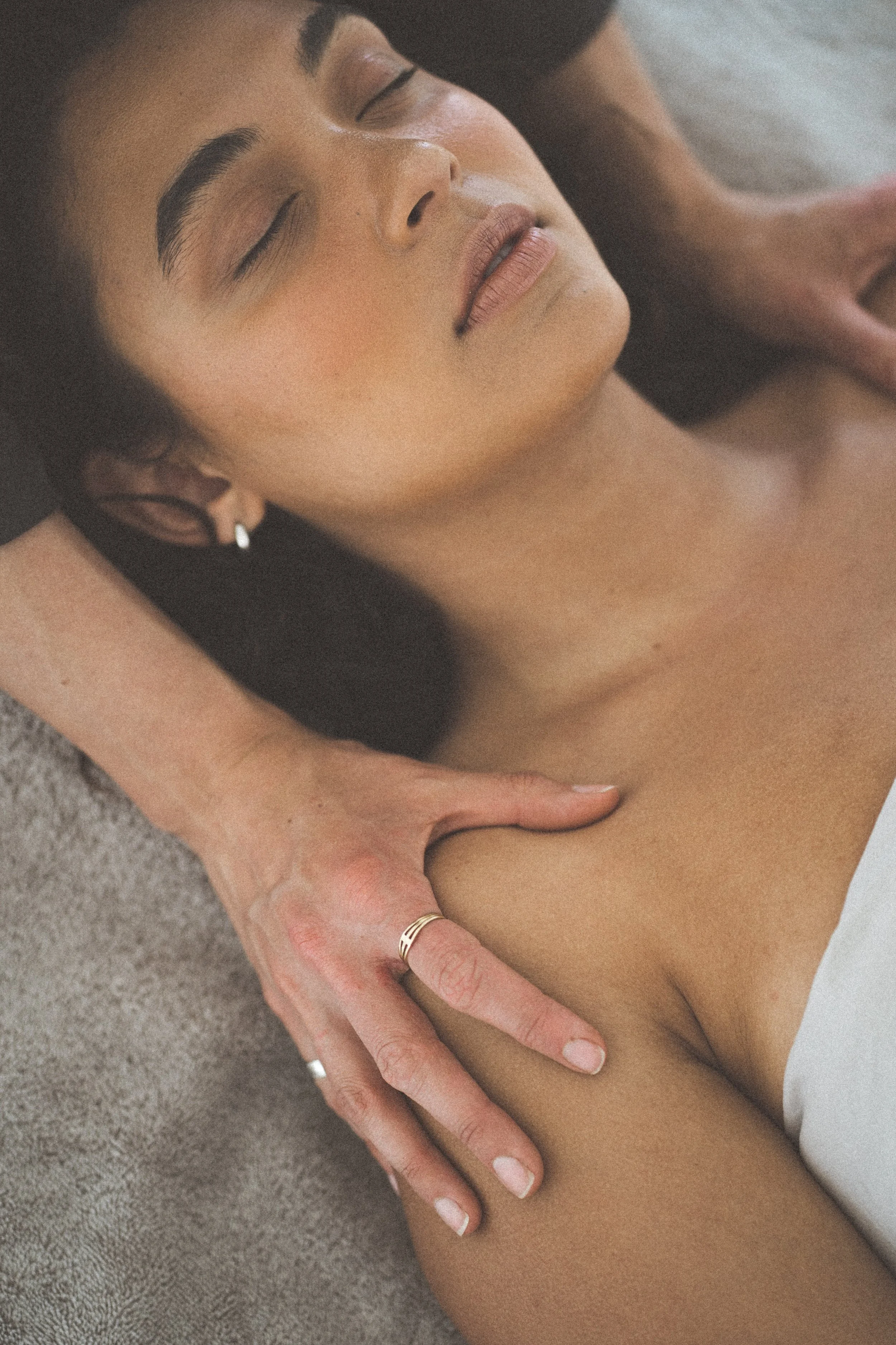 Close-up of a woman receiving a massage, with a focus on her face, neck, and shoulder area, lying on a textured surface, with her eyes closed and expression relaxing.