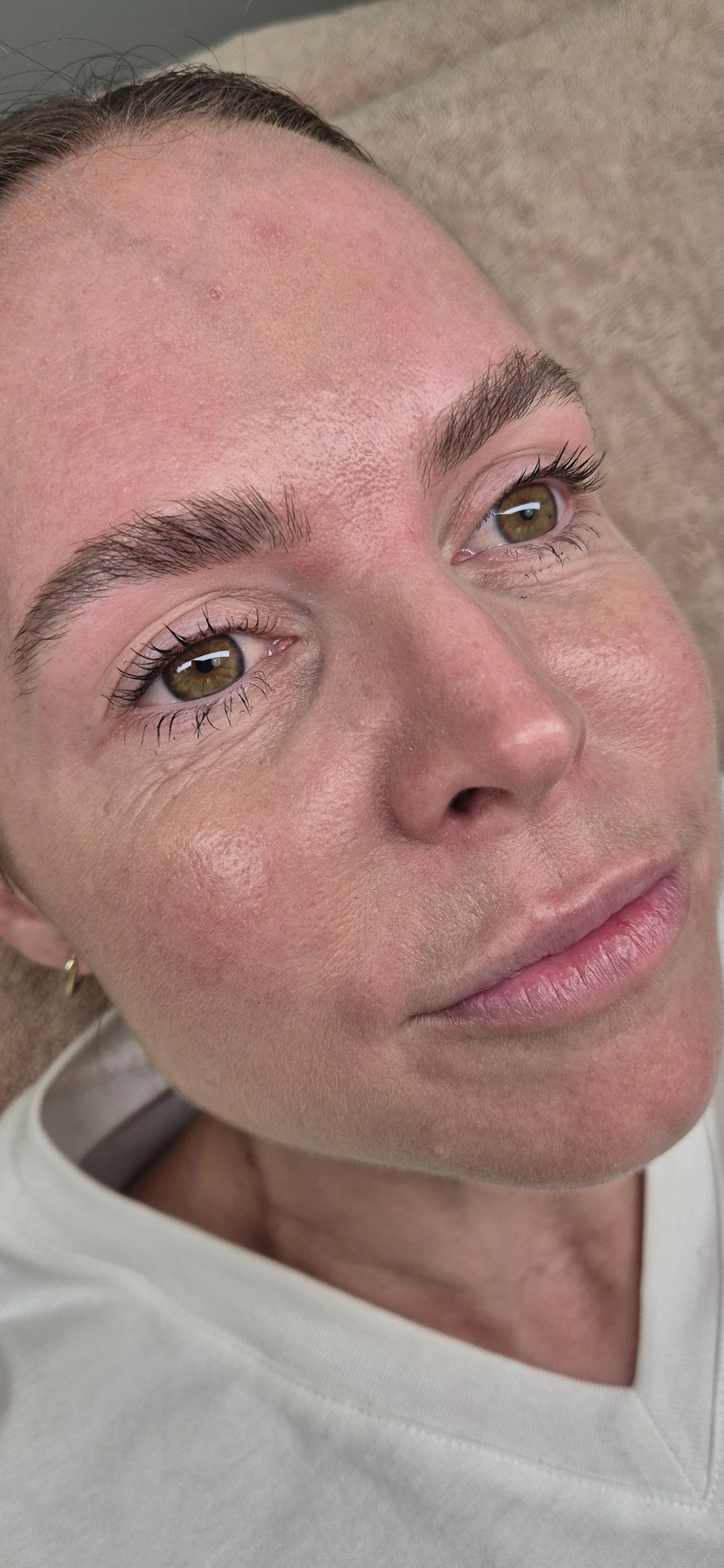 Close-up of a woman's face lying on a surface, showing her eyes, nose, and lips with natural makeup and slightly flushed cheeks.
