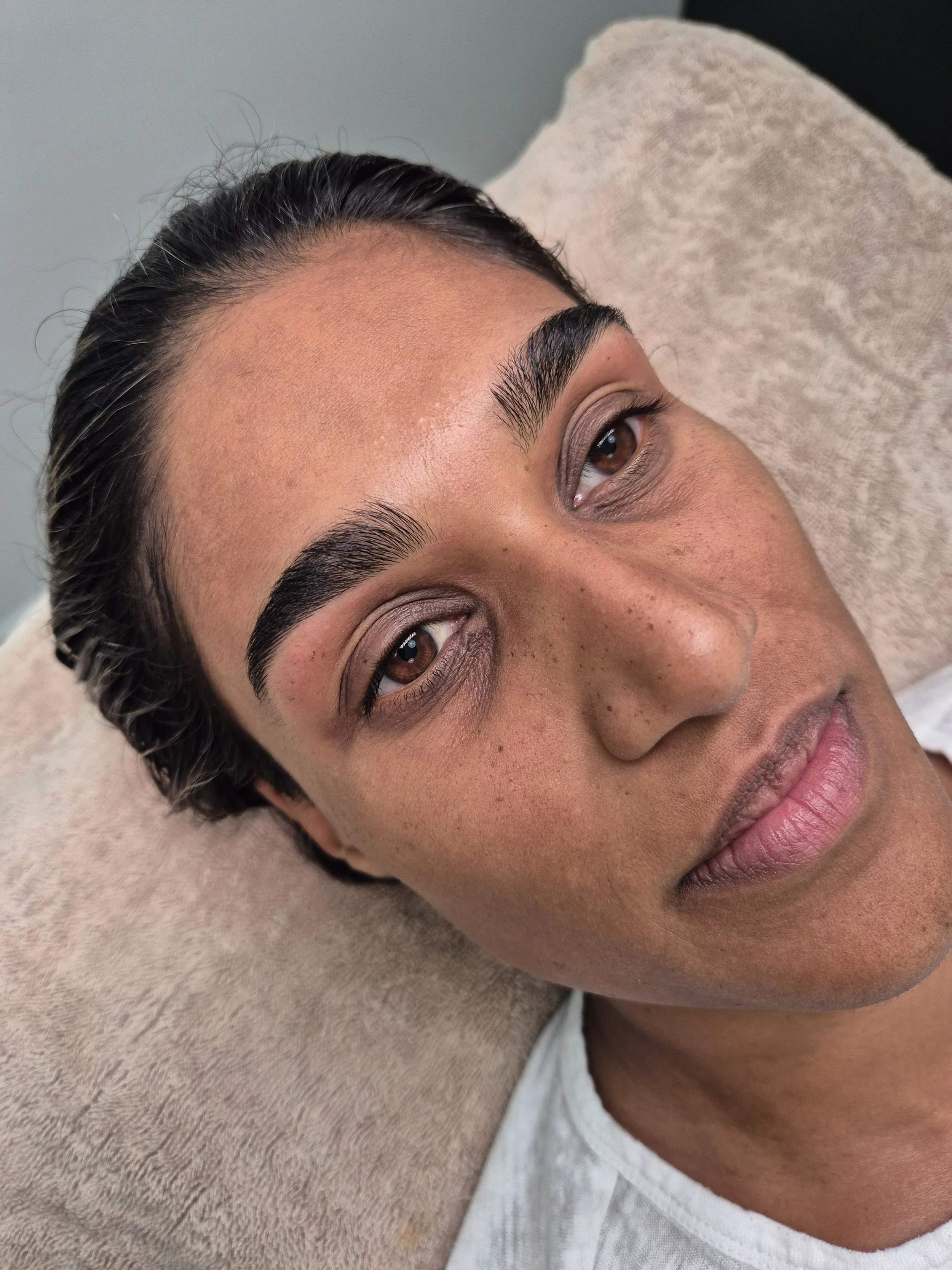 Close-up of a woman's face lying down with her eyes open, showing well-groomed eyebrows, long eyelashes, and natural skin texture.