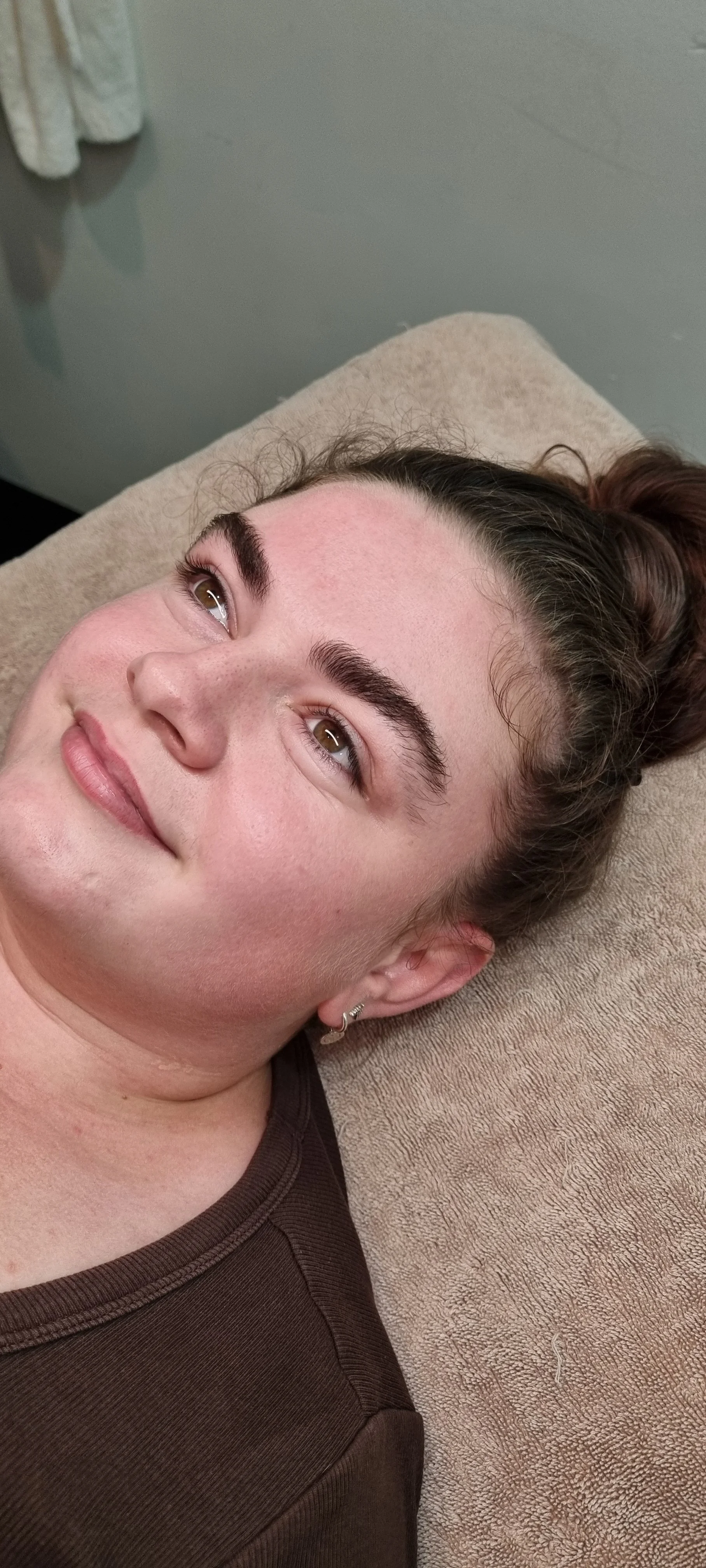 A woman with brown hair lying on a massage table, looking upwards, with a relaxed expression.