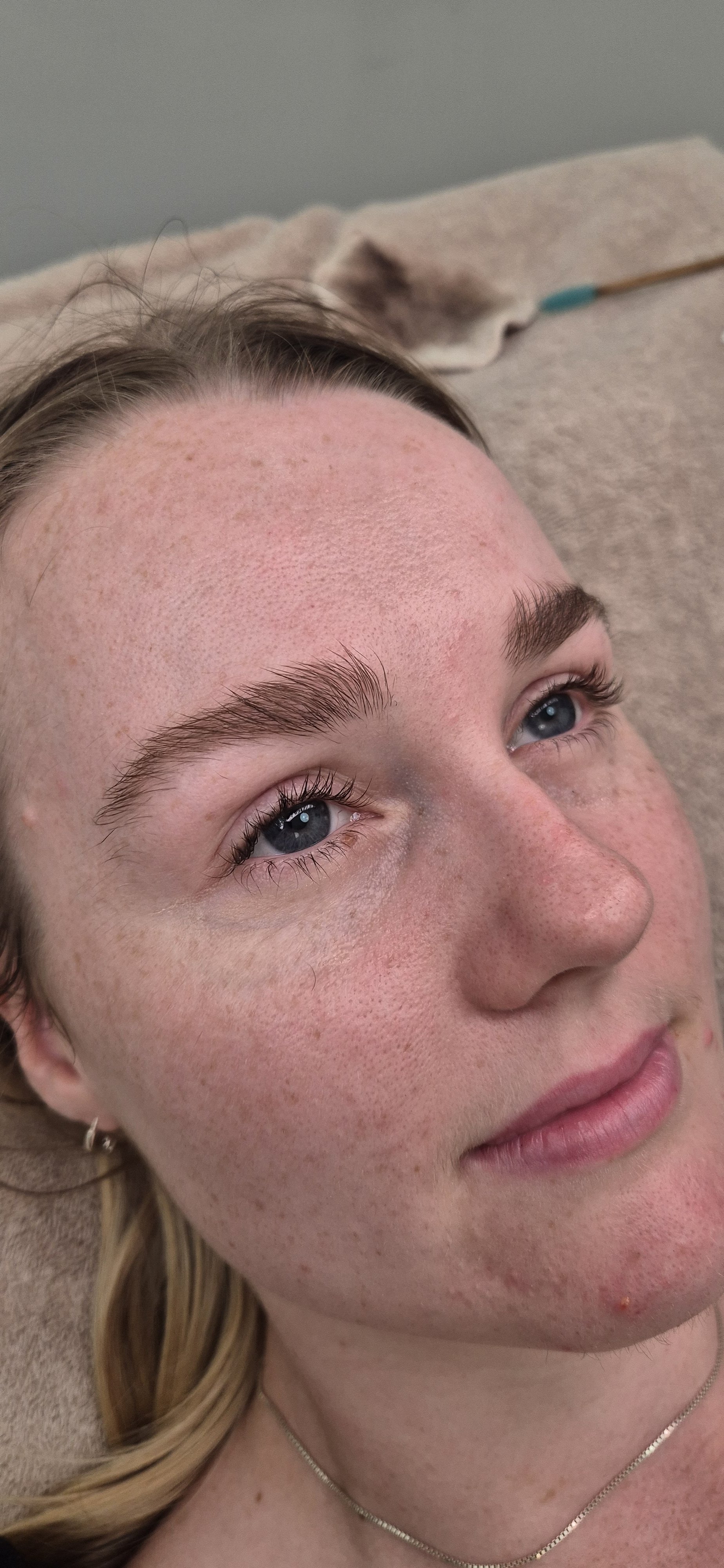 Close-up of a young woman lying down with visible freckles, blue eyes, and blonde hair, resting on a beige surface.