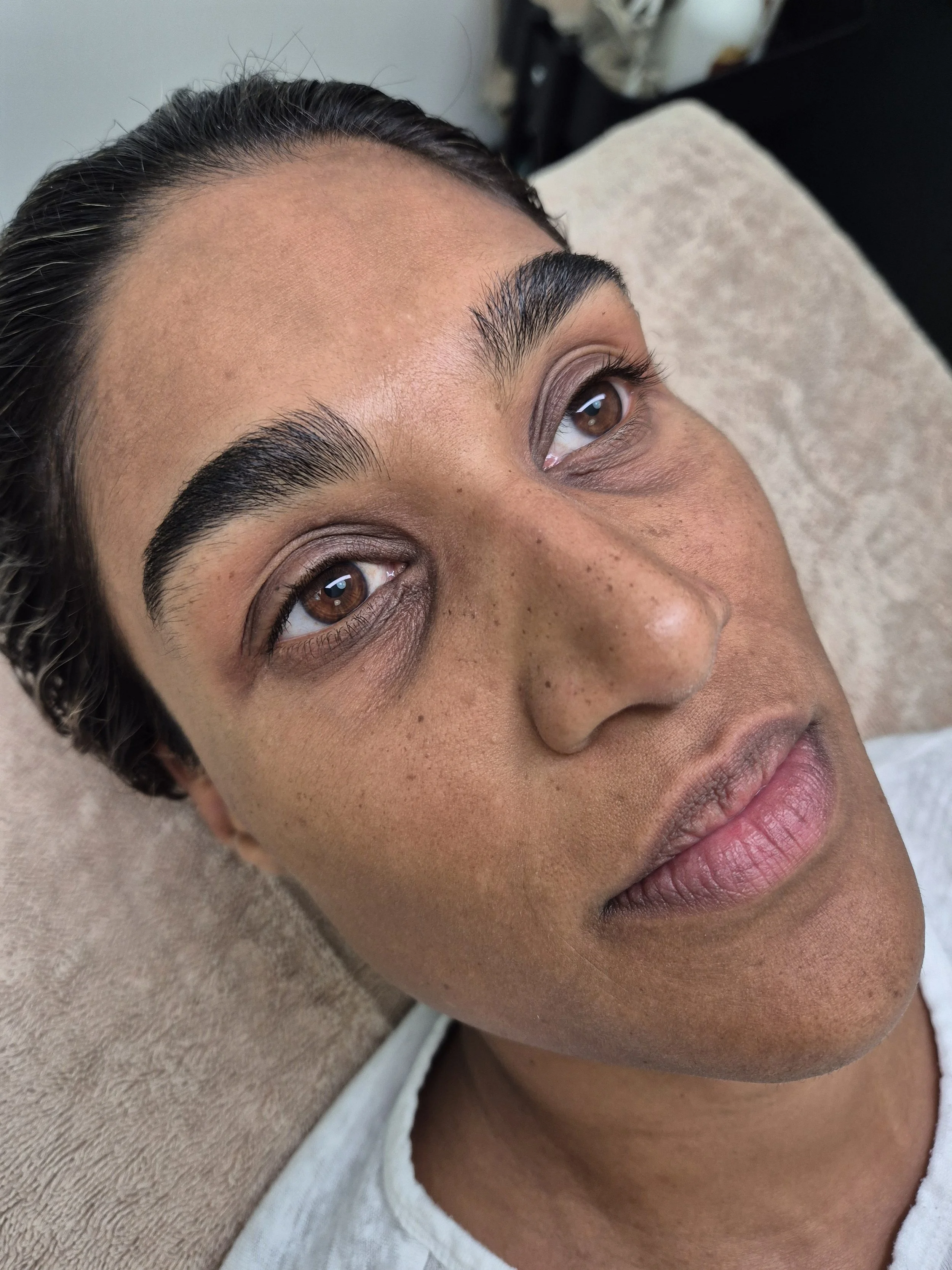 Close-up of a woman's face showing her eyebrows and eyes, as she appears to be lying down on a towel or soft surface.