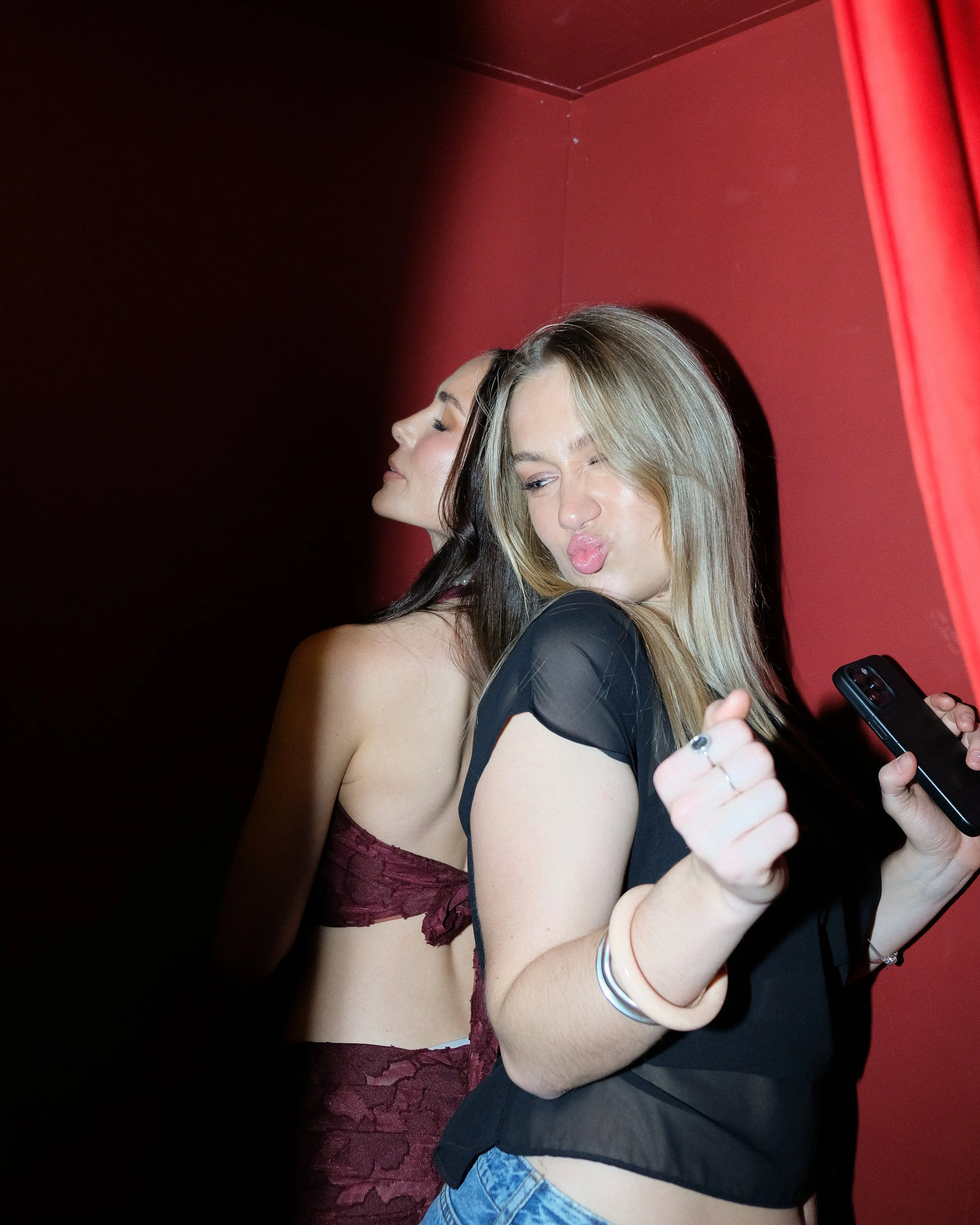 Two women embracing and taking a selfie inside a photobooth in Melbourne. One with blonde hair and the other with dark hair, both making playful expressions.