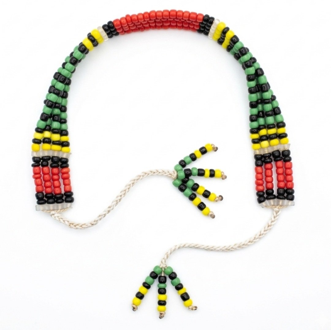 Handmade multi-row seed bead choker bracelet featuring a vibrant color-blocked geometric pattern in red, green, yellow, and black beads with white braided cord tie closures and matching beaded tassel ends, isolated on a white background.