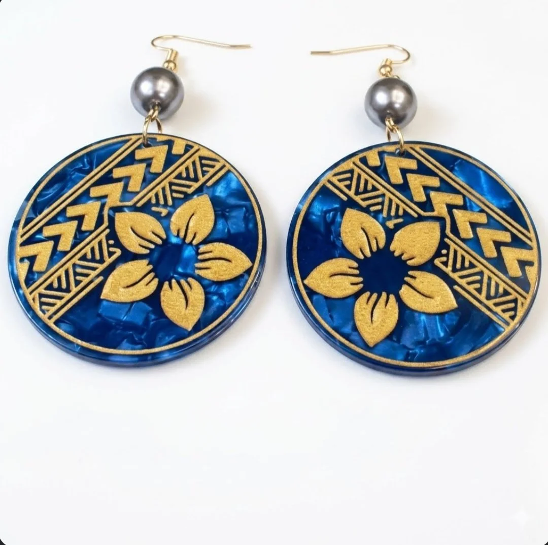 Pair of circular earrings with gold floral and geometric designs on blue background, featuring gray beads and gold hooks.