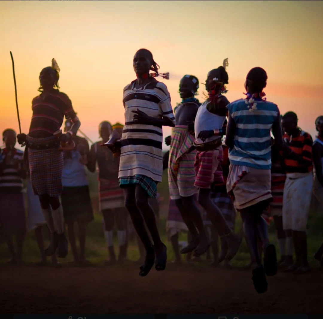 Group of Hamar people in colorful traditional clothing dancing Evan-Gadi in the air during sunset.