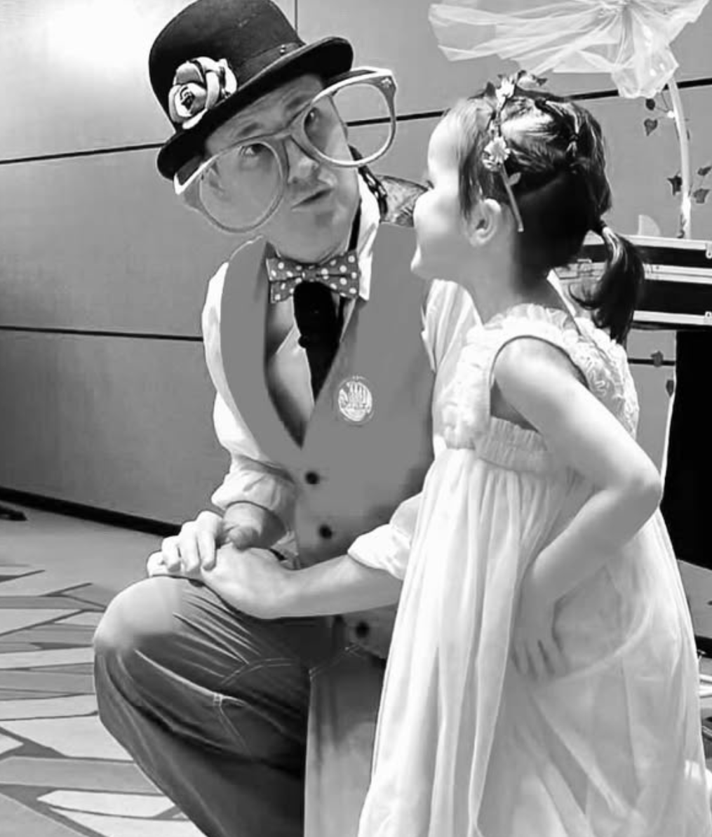 A woman and a performer in a clown costume share a moment, with the performer leaning close to the woman and holding her hand.