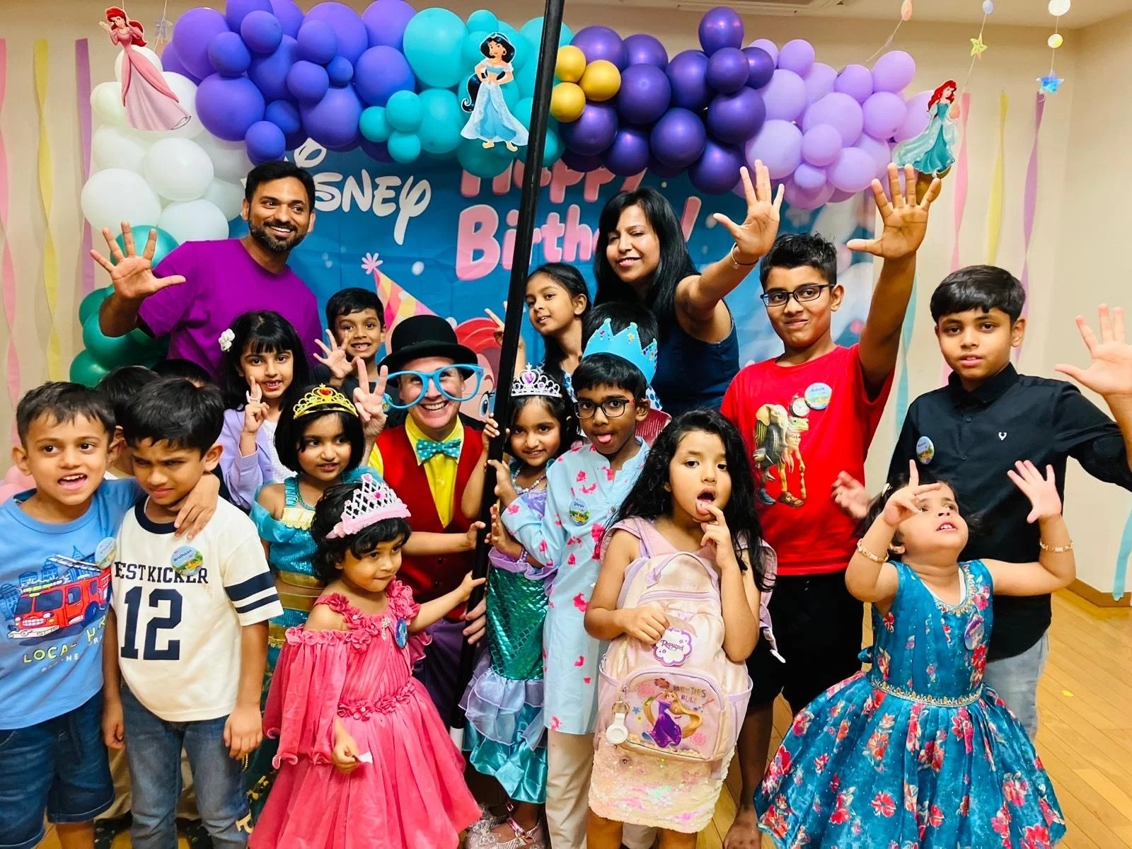 Children and adults celebrating a birthday with Disney princess decorations, balloons, and themed costumes.