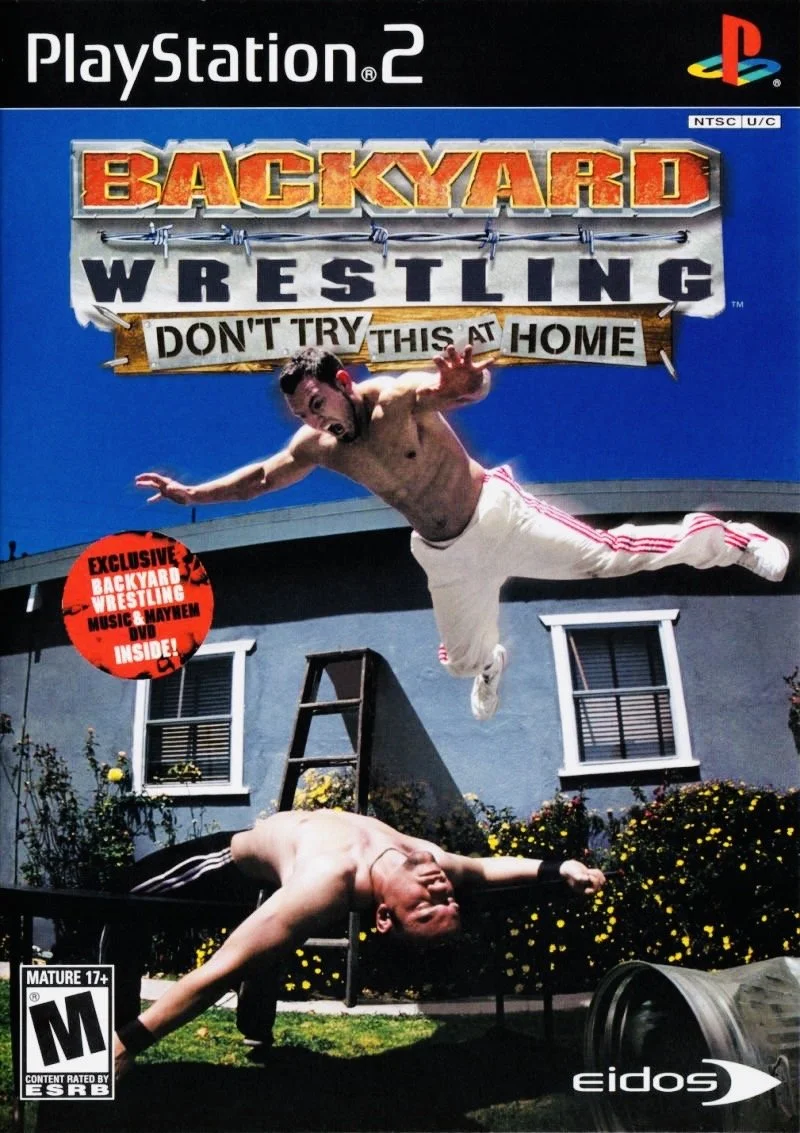 Video game cover titled "Backyard Wrestling" for PlayStation 2, showing two shirtless, muscled wrestlers outside a suburban house, one mid-air leaping off the roof onto the other drone on a table, with a sign that reads 'Don't Try This at Home'.