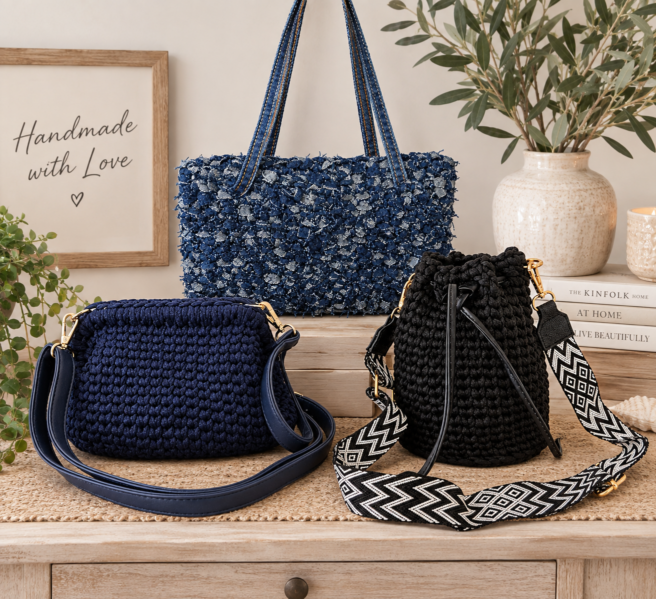 Three woven handbags in navy blue, black, and dark purple displayed on a wooden surface, with a framed sign, potted plant, and books in the background.