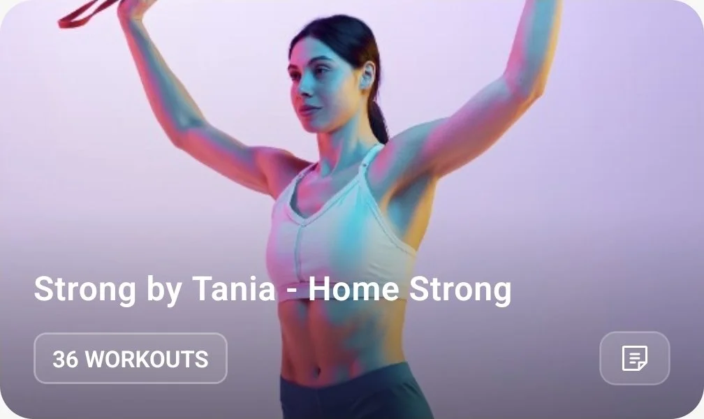 A woman in workout attire holding a resistance band overhead in a fitness studio with colorful lighting.