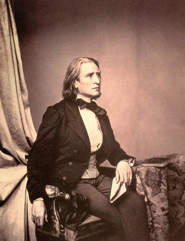 A woman with long hair, dressed in Victorian-style clothing, seated on an ornate sofa, holding a piece of paper, with a book resting on the arm of the sofa.