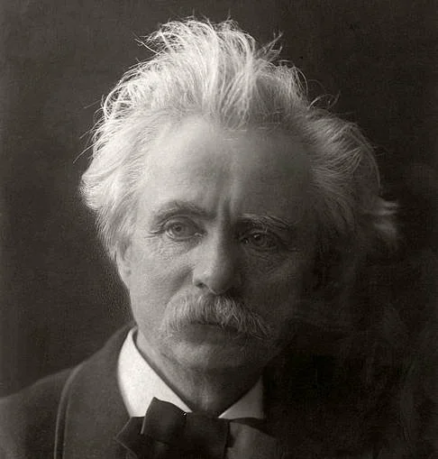 A black and white portrait of a man with wild, unkempt white hair, a mustache, and a serious expression, wearing a suit and bow tie.