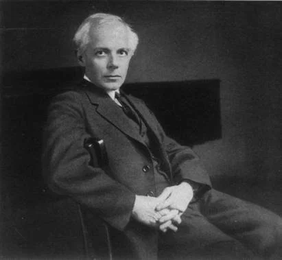 A black and white photograph of a man sitting in a chair, wearing a suit and looking towards the camera.