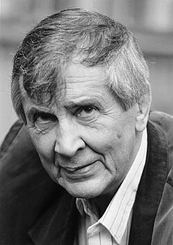 Black and white portrait of an older man with gray hair, dressed in a shirt and blazer, looking directly at the camera.