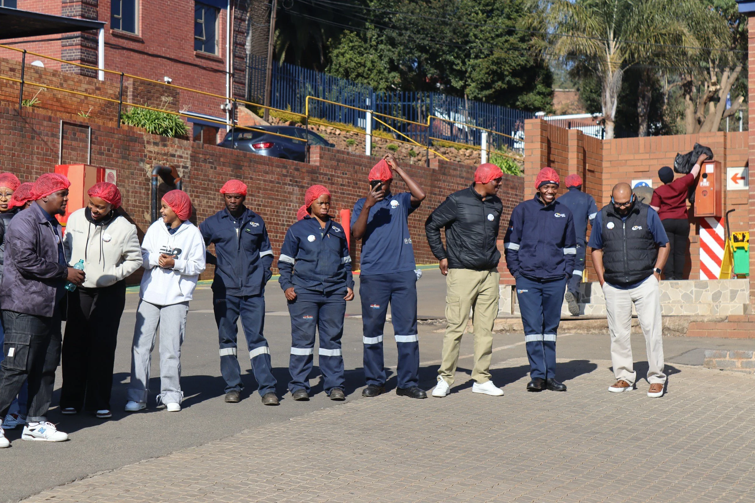 Group of people wearing red hair covers and dark clothing, standing outdoors near a brick wall, engaging in conversation and smiling.