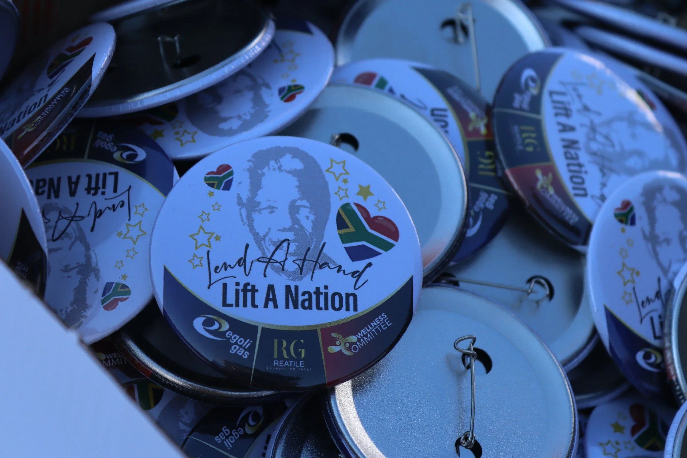 Close-up of multiple round badges with the South African flag, stars, and the text 'Lift A Nation.'