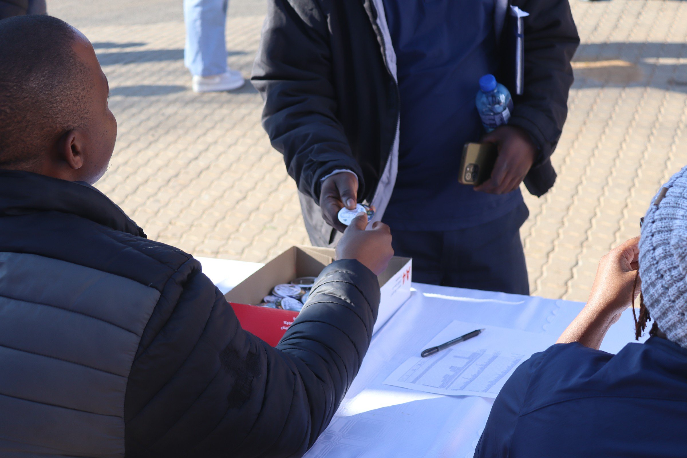 People exchanging items and signing documents at an outdoor table during the daytime.