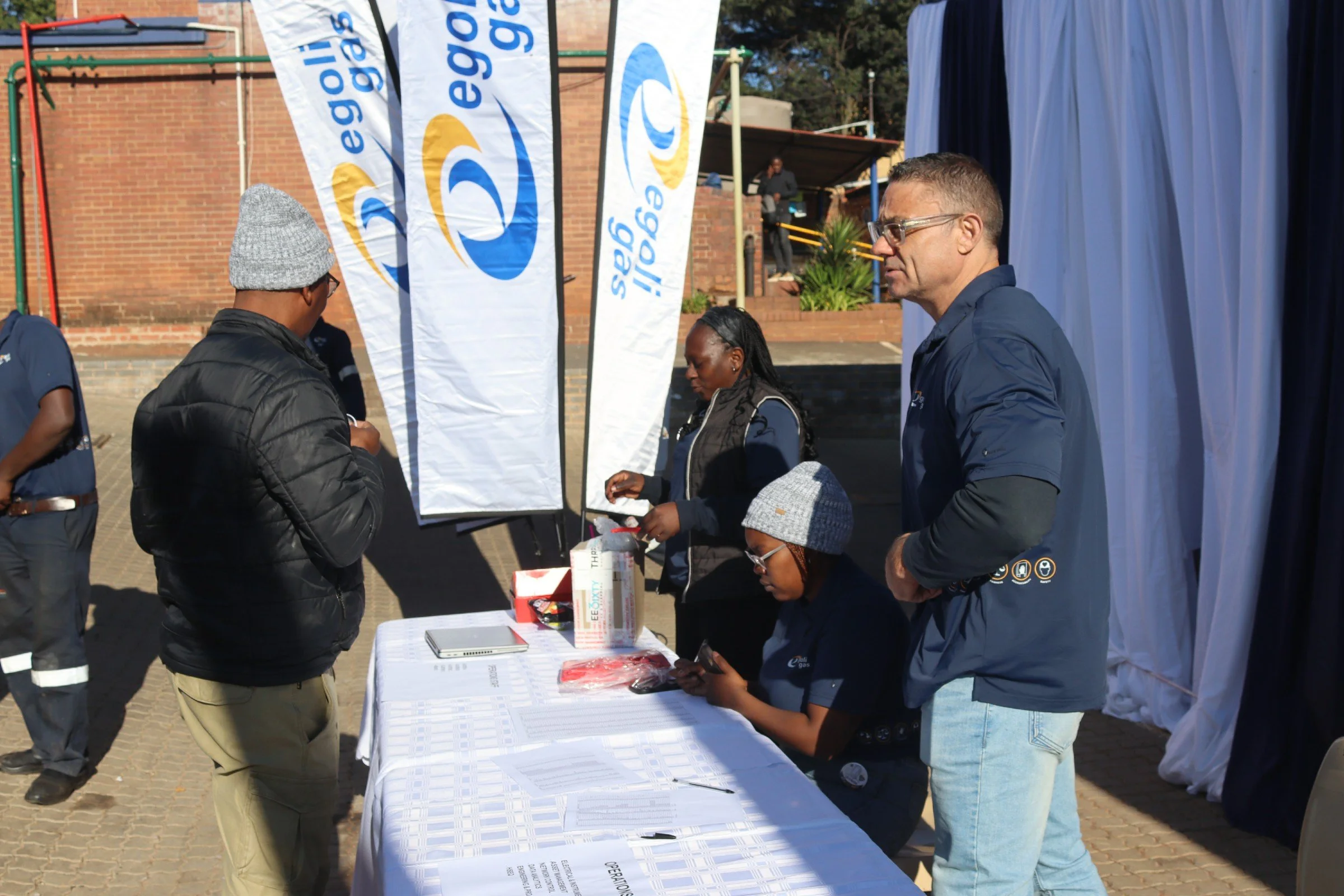 People standing around a table at an outdoor event with banners displaying 'eegas'.