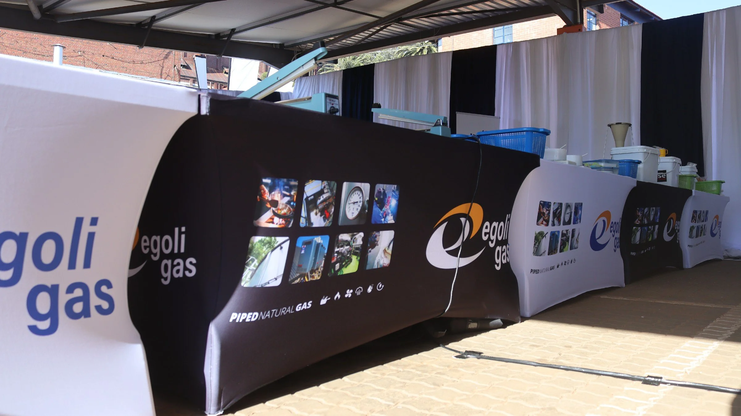Display booth with banners displaying Egoli Gas branding and images related to natural gas, set up outdoors under a canopy with a backdrop of brick buildings.