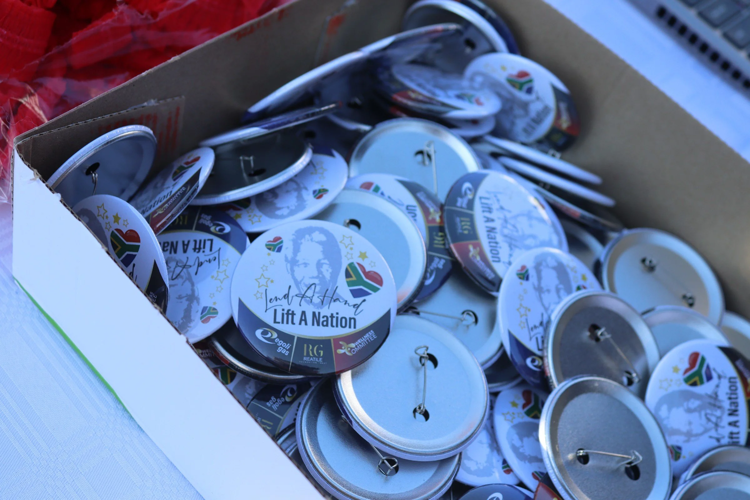 A cardboard box filled with circular buttons with ribbons and messages supporting lifting a nation.