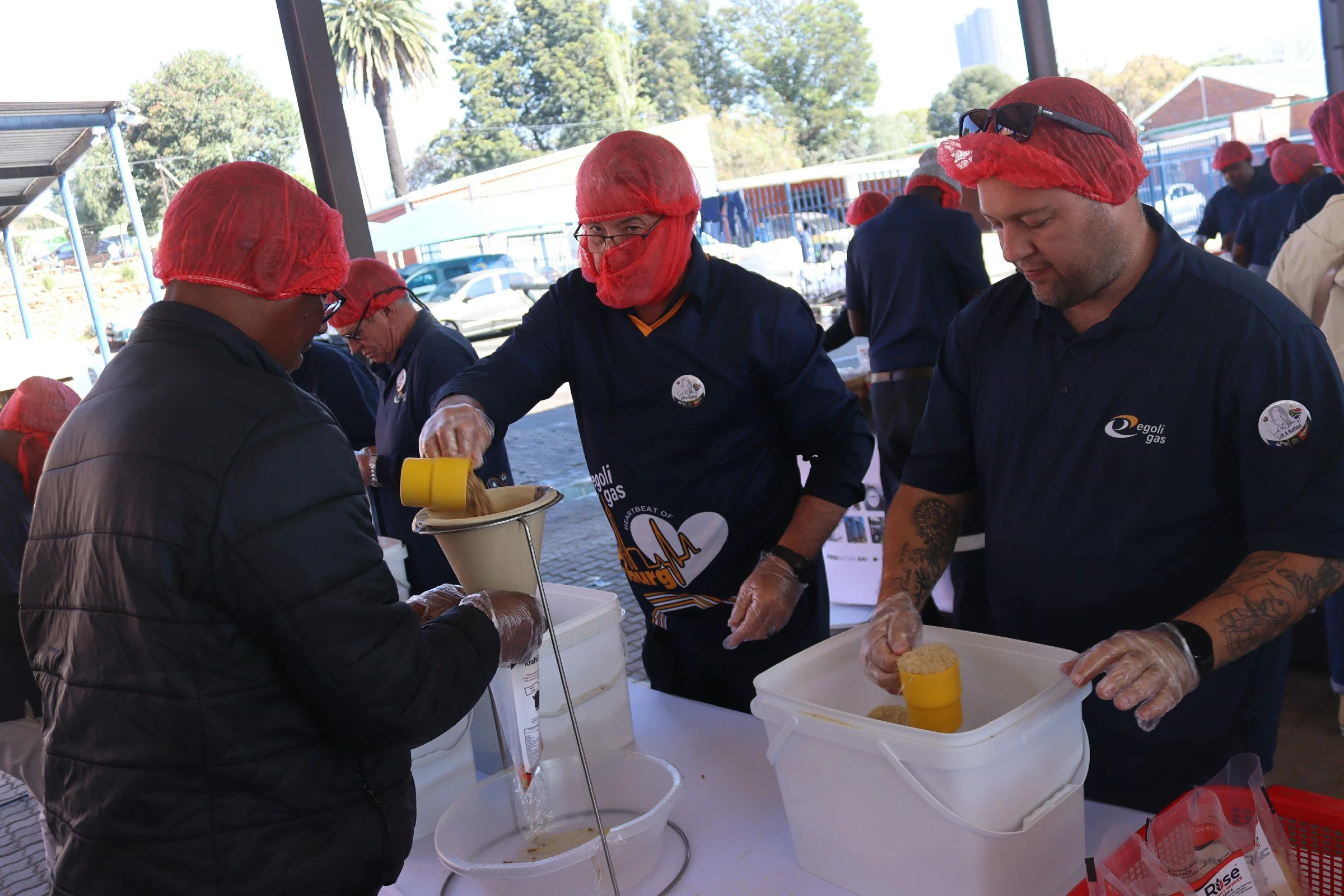 People wearing red hairnets and gloves preparing food at an outdoor event.