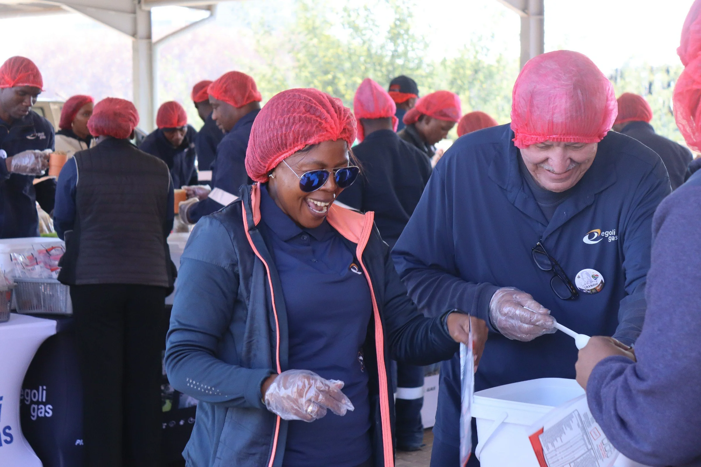 People wearing red hairnets and gloves serving food at an outdoor event.