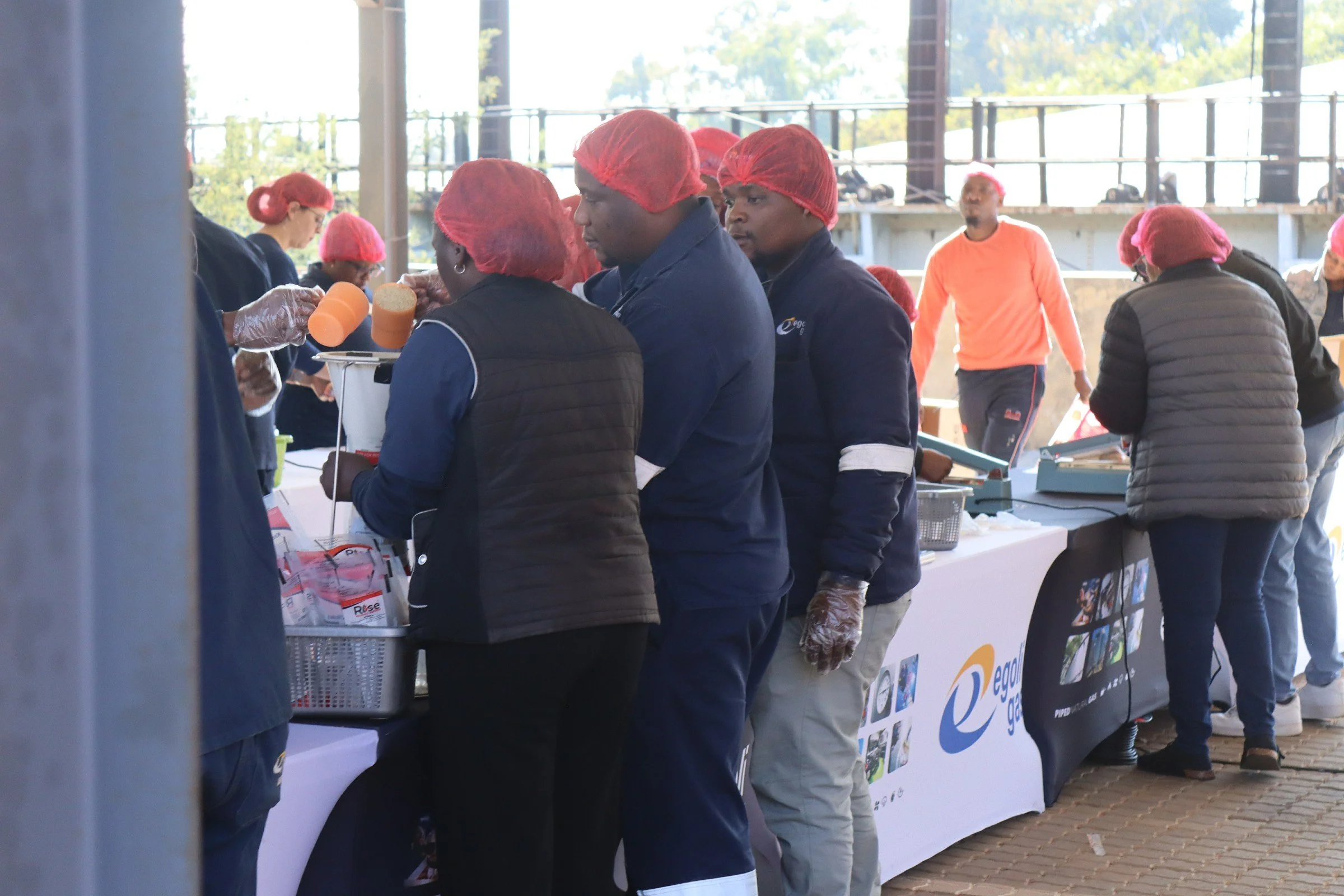 People wearing red hairnets and gloves standing in line at a food or product distribution booth.