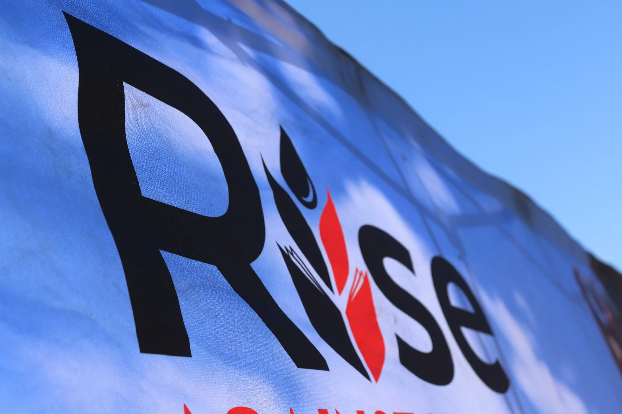 Close-up of a fabric banner with the Google logo, showing black, red, yellow, blue, and green colors, against a clear blue sky.
