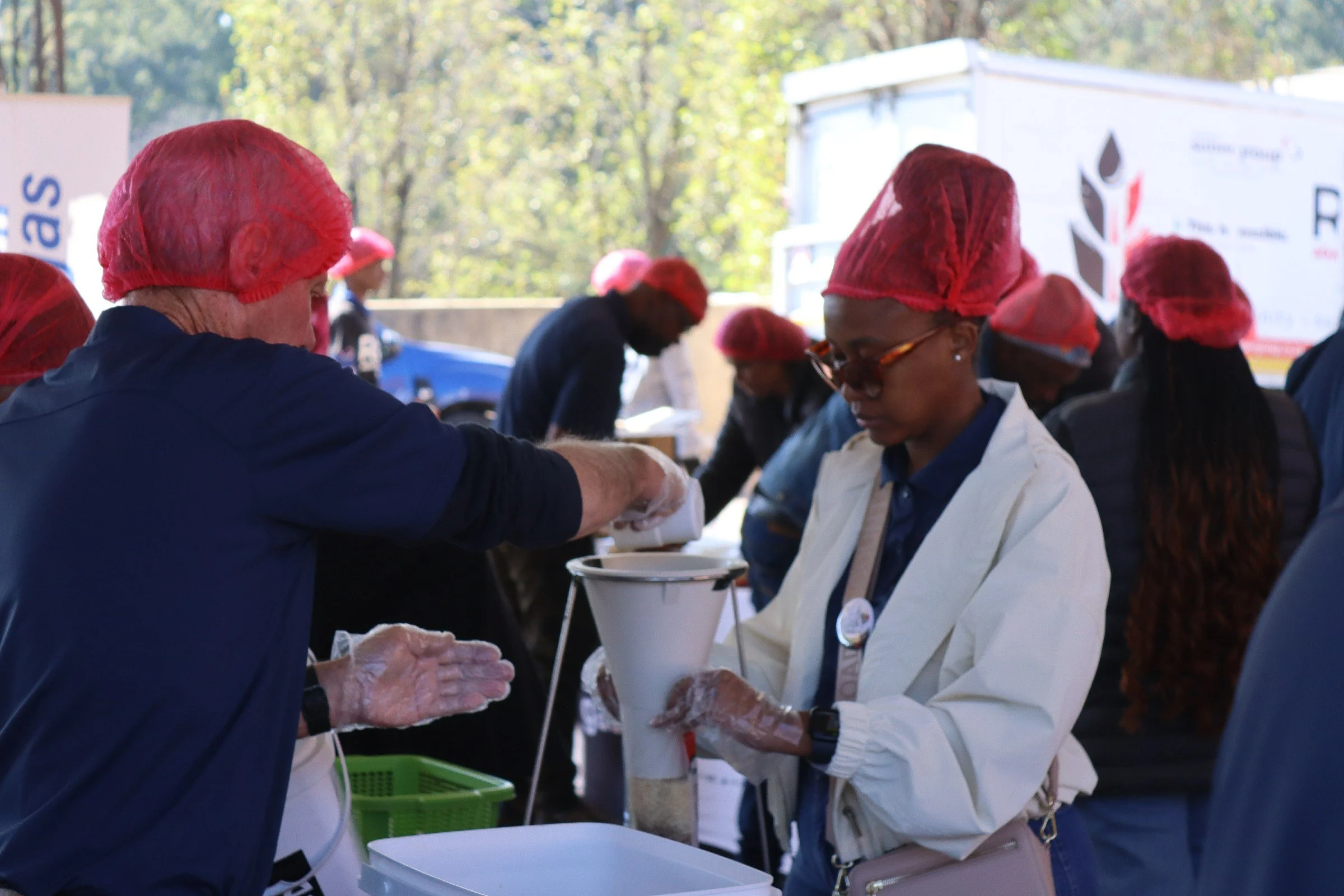 People wearing red hair nets and white uniforms working at an outdoor food service station.