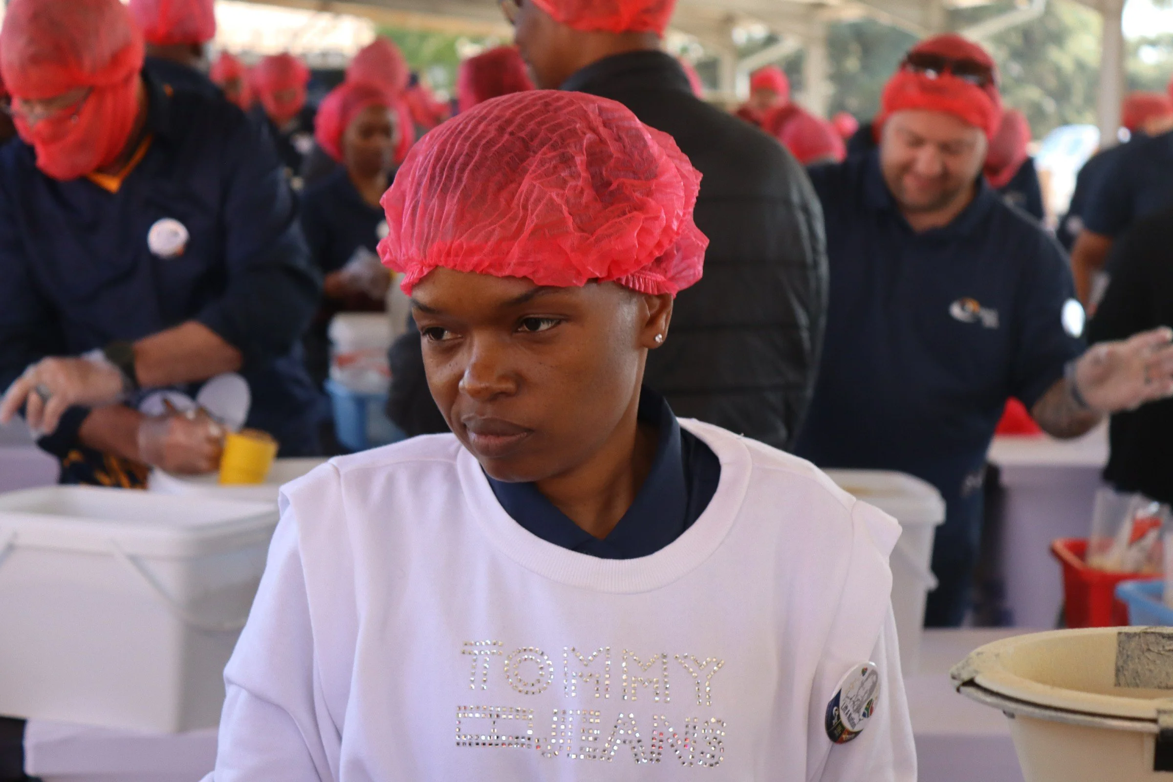 Person wearing a red hairnet and a white shirt with the word 'TUMMY' in rhinestones, participating in a group activity at a community event.