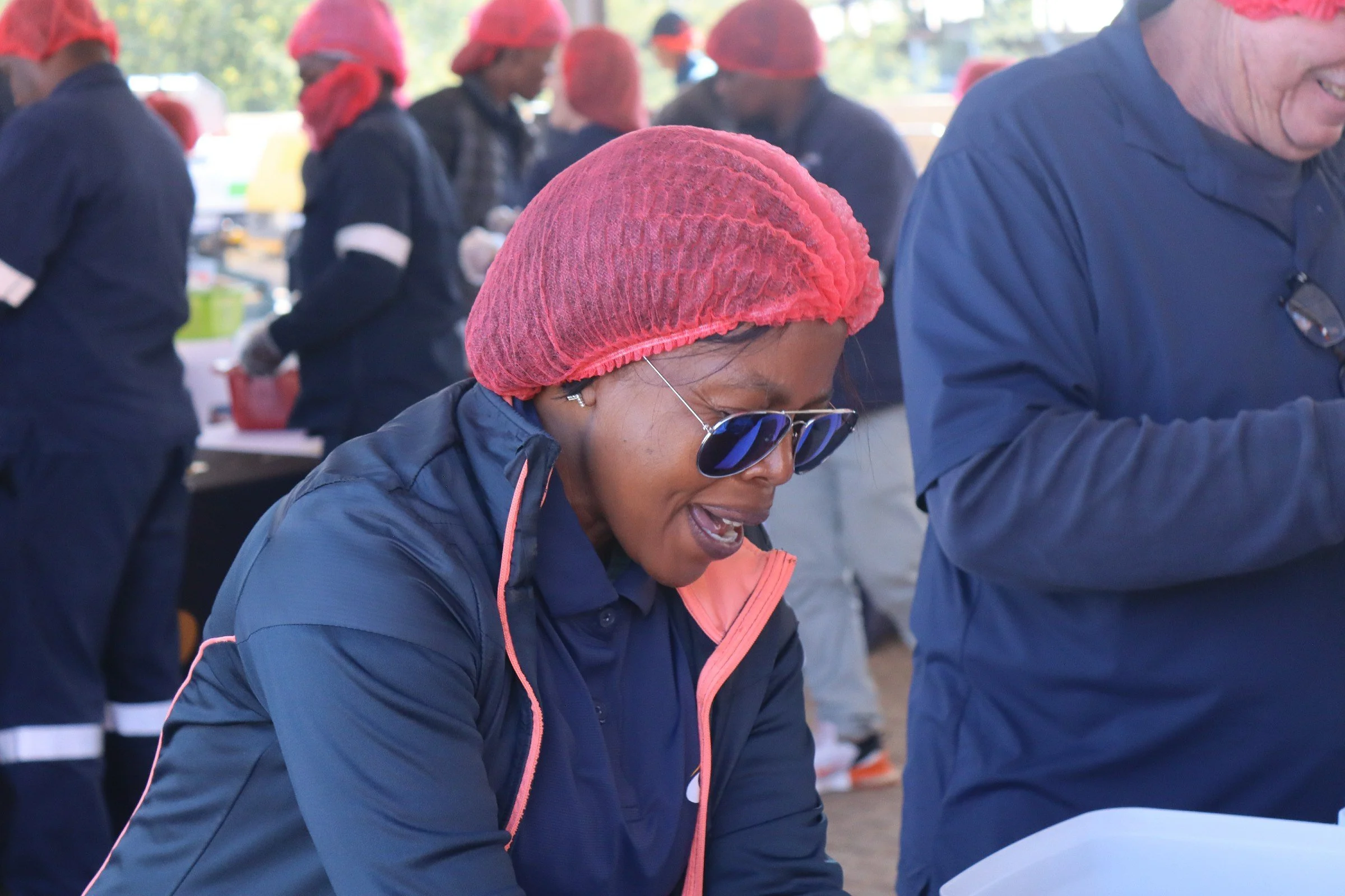 Group of people dressed in dark jackets and red hair covers, participating in an outdoor event or activity, some with sunglasses.