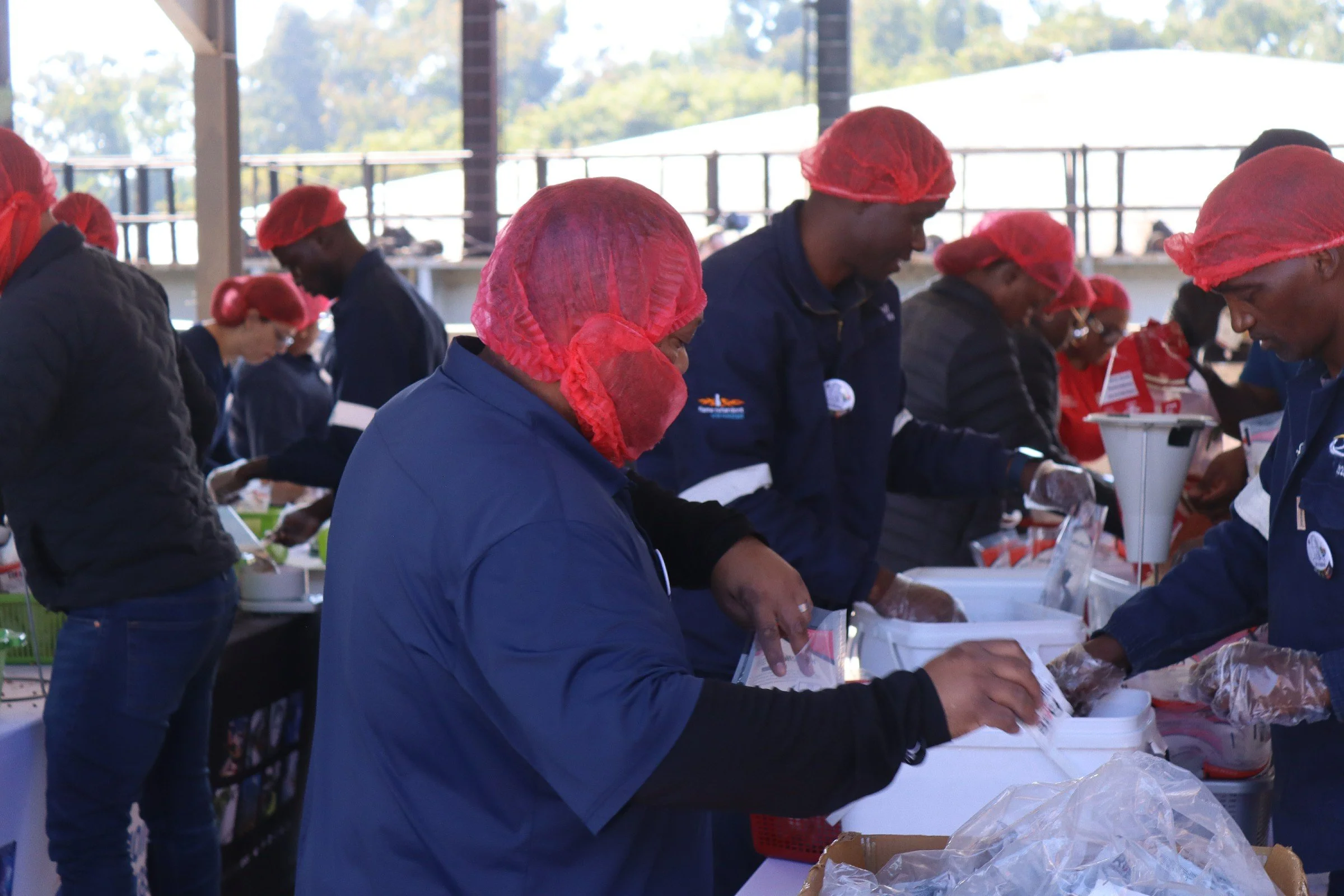 Group of people in red hairnets serving or preparing food in a large, open, well-lit space with a high ceiling and glass windows.