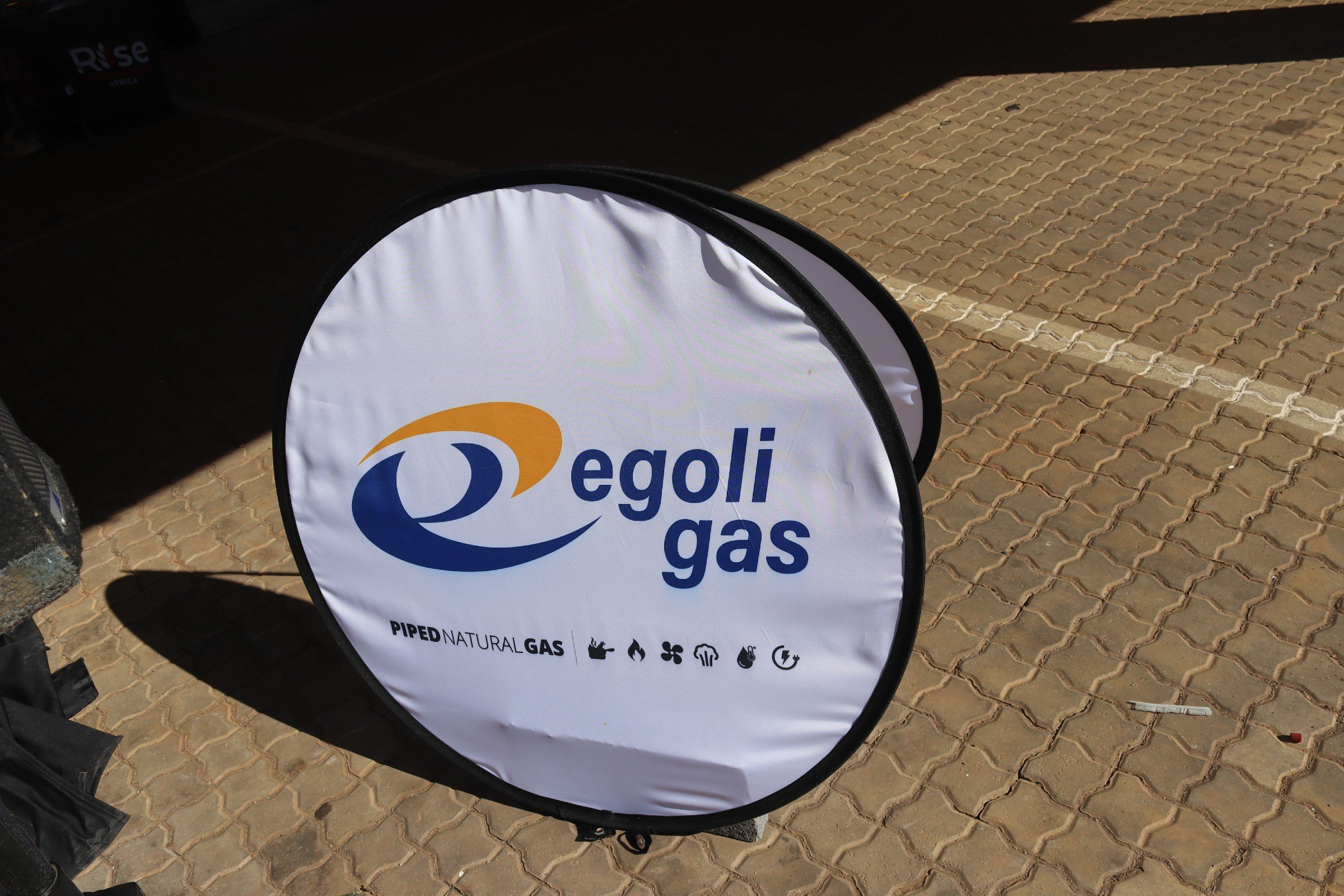 A round sign with the words "Egoli Gas" and icons representing natural gas, piping, flames, cooling, and electricity is placed on a paved parking lot.