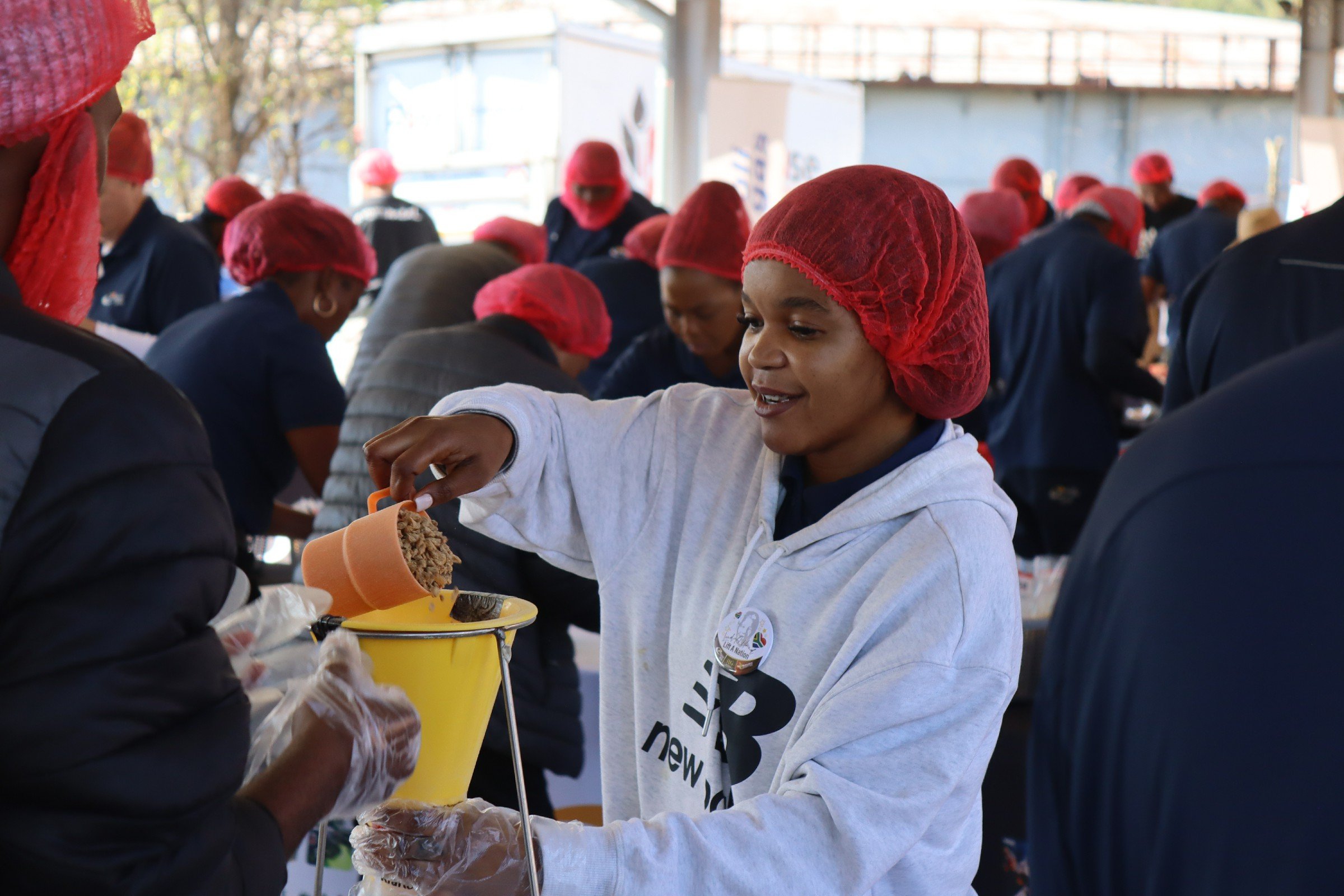A woman with a red hairnet and gray hoodie handing out food or supplies to people at a community event.