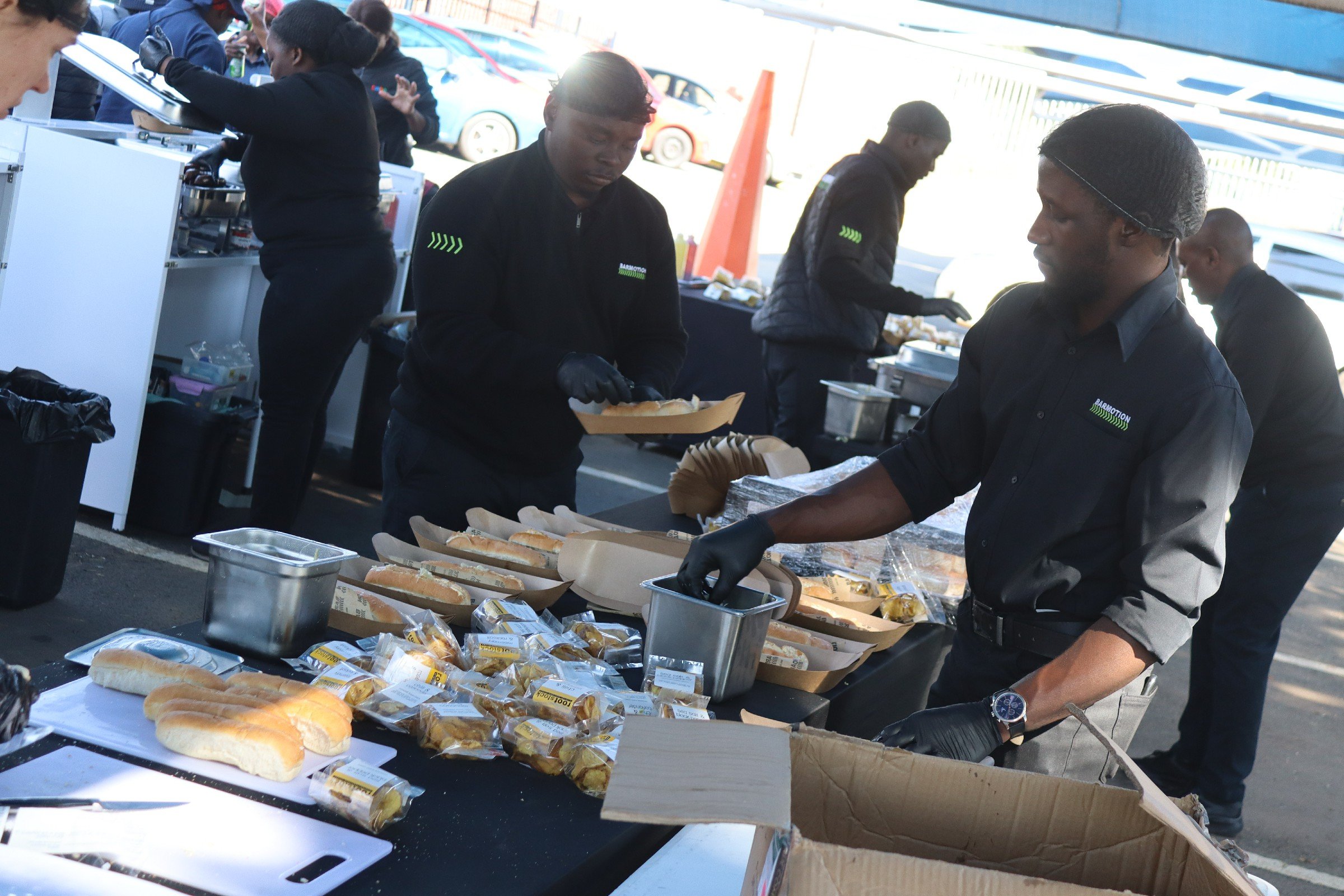 People serving hot dogs at a food distribution event outdoors.